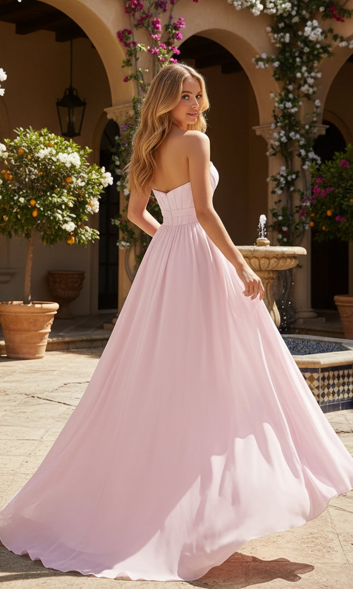 A woman wearing the Long Prom Dress: PromGirl Exclusive 250236B with an a-line chiffon skirt stands outdoors by a fountain and potted plants, glancing over her shoulder.
